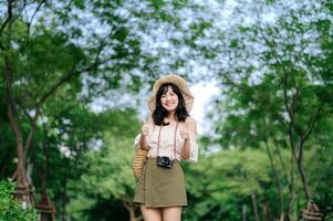 ritratto di asiatico giovane donna viaggiatore con tessitura cappello e cestino e un' telecamera su verde pubblico parco natura sfondo. viaggio viaggio stile di vita, mondo viaggio esploratore o Asia estate turismo concetto. foto