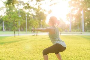 femmina pareggiatore. in forma giovane asiatico donna con verde abbigliamento sportivo allungamento muscolo nel parco prima in esecuzione e godendo un' salutare all'aperto. fitness corridore ragazza nel pubblico parco. benessere essere concetto foto