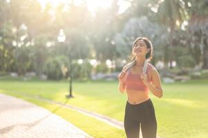 in forma contento Sorridi 30s giovane asiatico donna nel abbigliamento sportivo gode rinfrescante tramonto correre nel natura. il silhouette di figura contro il ambientazione sole è bellissimo vista. fitness, Salute, o motivazione concetto. foto