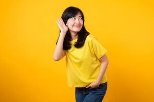 catturare Attenzione ritratto di giovane asiatico donna. indossare un' giallo maglietta e denim jeans, Leans nel per origliare e ascoltare, evocando curiosità e intrigo. cattura l'attenzione promozioni e sconti. foto