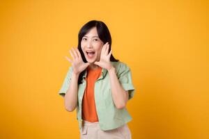 energico giovane asiatico donna nel sua 30s indossare un' verde camicia su un arancia sfondo, urlando con eccitazione. Esplorare il sconto shopping promozione concetto con Questo vivace Immagine. foto