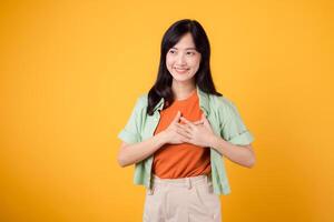 abbraccio il amore di offerte con un' giovane asiatico donna nel sua 30s indossare un' verde camicia su un arancia camicia, radiante felicità. amore affare promozione concetto contro un' vivace giallo sfondo. foto