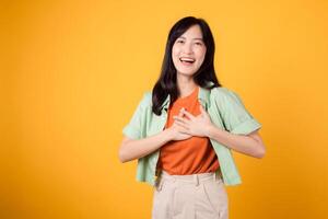 assistenza sanitaria e benessere con un asiatico giovane donna nel sua anni '30, indossare un' verde camicia. lei vetrine un' mano gesto su sua il petto contro un' giallo sfondo, incarnando il concetto di corpo benessere. foto