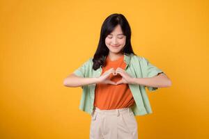 assistenza sanitaria e benessere di un asiatico donna nel sua 30s indossare un' verde camicia. sentire il trasformativo energia di sua cuore mano gesto su un' vivace giallo sfondo, accensione il sentiero per corpo benessere. foto