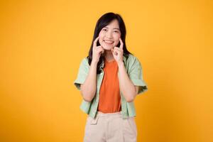 dentale igiene con delizioso giovane asiatico donna anni '30, elegantemente rivestito nel arancia camicia e verde Maglione punti per sua denti su un' giallo sfondo, evidenziazione il significato di dentale assistenza sanitaria. foto