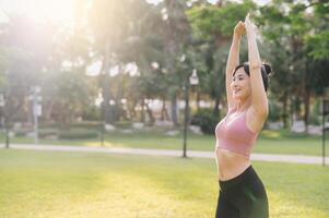 benessere e salutare stile di vita ritratto di 30s asiatico donna nel rosa abbigliamento sportivo. preparare e allungare braccio muscoli prima tramonto correre nel il parco. fitness al di fuori e vivere un' equilibrato vita. foto