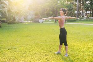 femmina pareggiatore. in forma 30s giovane asiatico donna nel rosa abbigliamento sportivo preparazione caldo su corpo nel parco prima correre. salutare all'aperto stile di vita con fitness corridore ragazza nel tramonto. concetto di benessere e benessere foto