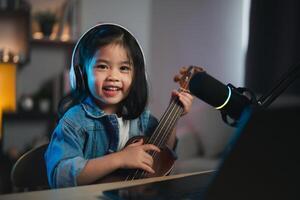 asiatico giovane ragazza sorridente vivere streaming prestazione giocando ukulele e cantare un' canzone. asiatico ragazza apprendimento chitarra e cantando in linea. musicista registrazione musica con il computer portatile e giocando acustico chitarra. foto