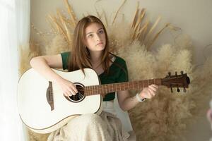 ritratto di adolescenziale ragazza con lungo capelli nel verde vestito giocando acustico chitarra. foto