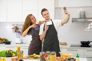 giovane coppia amante cucinando insieme nel il cucina a casa. contento coppia assunzione autoscatto con smartphone. foto