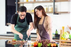 un' giovane coppia indossare grembiule molto contento dopo porzione per rendere un' bistecca a il cucina nel loro casa, Sorridi, e guardare il bistecca su un' di legno piatto foto