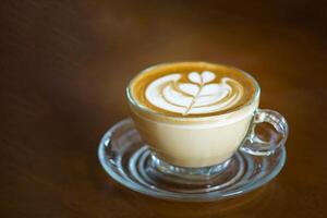 avvicinamento di caffè tazza con cuore forma latte macchiato arte schiuma su di legno tavolo. foto