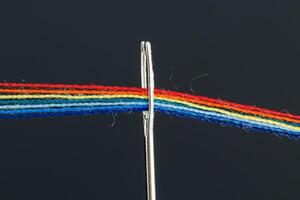 multicolore discussioni per cucire nel il modulo di un' arcobaleno passaggio attraverso un antico ago su un' nero sfondo foto