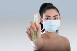 giovane donna asiatica che indossa una maschera medica n95 con la mano che applica spray alcolico dalla bottiglia di plastica o anti batteri per prevenire la diffusione di germi su sfondo grigio foto