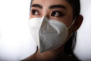 primo piano di una giovane donna asiatica che indossa una maschera medica per proteggersi dalle malattie respiratorie trasmesse dall'aria come l'influenza covid-19 pm2.5 polvere e smog su sfondo grigio, concetto di infezione da virus di sicurezza