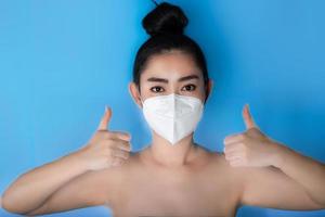 primo piano di una donna che indossa una maschera respiratore n95 per proteggersi dalle malattie respiratorie trasmesse dall'aria come l'influenza covid-19 corona pm2.5 polvere e smog, gesto femminile di pollice in su con la mano