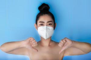 primo piano di una donna che indossa una maschera respiratore n95 per proteggersi dalle malattie respiratorie trasmesse dall'aria come l'influenza covid-19 corona pm2.5 polvere e smog, gesto femminile pollice giù con la mano
