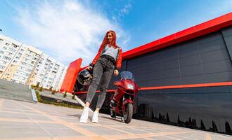 un' elegante donna e sua vivace rosso motociclo. un' donna in piedi Il prossimo per un' rosso motociclo foto