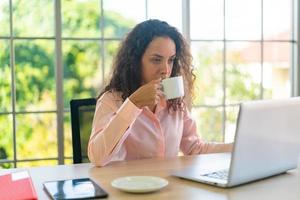 donna latina che lavora con una tazza di caffè sullo spazio di lavoro foto