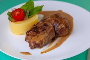 Manzo cotolette Polpette con schiacciato patate su un' bianca piatto. carne nel acida crema salsa. pomodori e basilico. cibo nel il ristorante. pranzo porzione. medaglioni foto