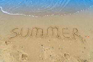 il parola estate è scritto su il giallo sabbia di il spiaggia. blu onda e Surf. ricorrere e vacanza. estate su il mare. rilassamento riposo concetto foto