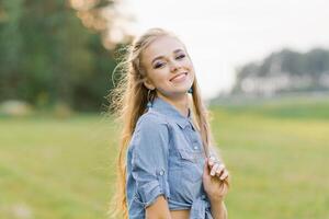 giovane caucasico donna, un' adolescenziale ragazza, un' alunno passeggiate nel il parco nel il estate, nel il foresta all'aperto, guardare in il telecamera foto