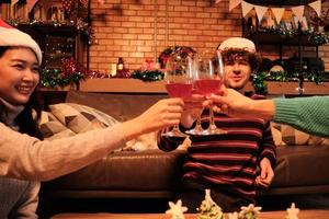 la famiglia e gli amici della felicità stanno festeggiando, alzando i bicchieri e un sorriso allegro con bevande e cane dietro nel soggiorno di casa, decorato per la festa di Natale e il giorno di Capodanno. foto