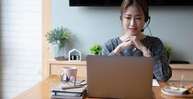 ritagliata colpo sorridente freelance donna asiatica che indossa l'auricolare, comunicando con il cliente tramite chiamata computer video. tutor femminile professionale millenario piacevole che tiene lezioni di lingua online foto