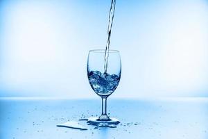 raccolta di spruzzi d'acqua in un bicchiere di vino isolato su sfondo blu foto