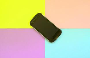 lo smartphone nero antiurto giace su uno sfondo color pastello foto