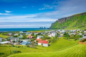 vista di pile di basalto reynisdrangar, spiaggia di sabbia nera vulcanica e lupino viola e fiori di prato gialli nella città di vik, nel sud dell'Islanda, in estate giornata di sole e cielo blu. foto