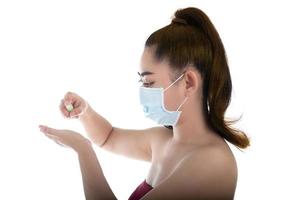 giovane donna asiatica che indossa una maschera medica n95 con la mano che applica spray alcolico dalla bottiglia di plastica o anti batteri per prevenire la diffusione di germi su sfondo bianco