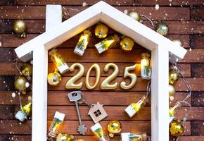 Casa chiave con portachiavi Villetta su festivo Marrone di legno sfondo con stelle, luci di ghirlande. nuovo anno 2025 d'oro lettere sotto il tetto. Acquista, costruzione, trasloco, mutuo, assicurazione foto