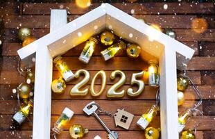 Casa chiave con portachiavi Villetta su festivo Marrone di legno sfondo con stelle, luci di ghirlande. nuovo anno 2025 d'oro lettere sotto il tetto. Acquista, costruzione, trasloco, mutuo, assicurazione foto
