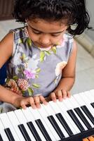 asiatico carino ragazza giocando il sintetizzatore o pianoforte. carino poco ragazzo apprendimento Come per giocare pianoforte. del bambino mani su il tastiera interno. foto