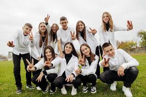 un' gruppo di molti contento adolescenti vestito nel il stesso attrezzatura avendo divertimento e in posa nel un' stadio vicino un' Università. concetto di amicizia, momenti di felicità. scuola amicizia foto