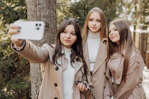 tre giovane donne assunzione autoscatto con inteligente mobile Telefono all'aperto - contento bellissimo femmina amici sorridente a telecamera all'aperto - stile di vita concetto con allegro ragazze godendo all'aperto vacanza. foto