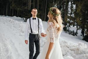 il sposa e sposo siamo in esecuzione lungo un' nevoso strada contro il sfondo di un' pino foresta e bellissimo contrasto luce del sole. lato Visualizza. inverno nozze. posto per logo. foto