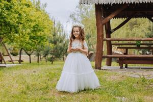 poco biondo ragazza con fiori su sua testa, nel un' bianca vestire, Tenere nozze anelli per il nozze cerimonia. primavera nozze foto