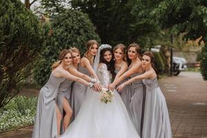 gruppo ritratto di il sposa e damigelle. un' sposa nel un' nozze vestito e damigelle d'onore nel argento vestiti hold elegante mazzi di fiori su loro nozze giorno. foto