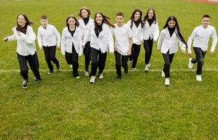 un' gruppo di molti contento adolescenti vestito nel il stesso attrezzatura avendo divertimento e in posa nel un' stadio vicino un' Università. concetto di amicizia, momenti di felicità. scuola amicizia foto