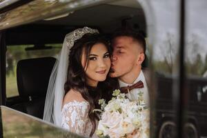 bellissimo sposa e sposo baci mentre seduta nel un' macchina. un' bellissimo sposa con un' mazzo di fiori nel sua mani è seduta nel un' elegante costoso macchina. foto