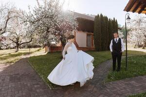 il sposa è girando nel sua nozze vestire, e il sposo è guardare a suo. nozze foto sessione nel un' bellissimo primavera parco.