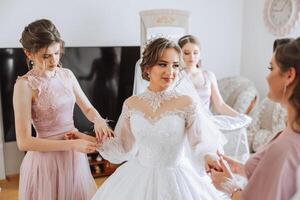 mattina di il sposa. il della sposa domestica di onore aiuta il sposa pizzo su sua vestire, allacciare pulsanti su il vestito o maniche. amiche Aiuto il sposa allacciare sua vestito foto