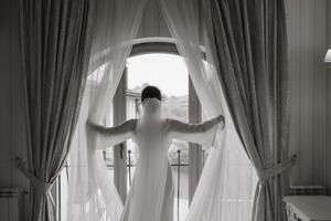 posteriore Visualizza di donna in piedi vicino finestra di moderno lusso appartamento o Hotel camera. nero e bianca foto