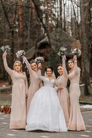 un' brunetta sposa nel un' bianca elegante vestito e sua amici nel grigio vestiti posa con mazzi di fiori. nozze ritratto nel natura, nozze foto nel leggero colori.
