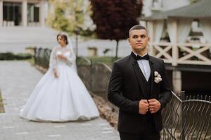 un' bello sposo nel un' primavera parco è in piedi nel davanti di il suo sposa. bellissimo nozze bianca vestire. passeggiate nel il parco. un' contento e amorevole coppia. foto