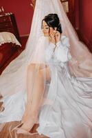un' bellissimo brunetta sposa con un' tiara nel sua capelli è ottenere pronto per il nozze nel un' bellissimo accappatoio nel boudoir stile. avvicinamento nozze ritratto, foto. foto