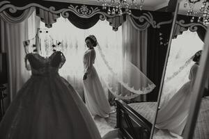 un' contento sposa è preparazione per sua lussuoso nozze nel un' Hotel camera, con un' nozze vestito su un' indossatrice qui vicino. ritratto di un' donna con alla moda capelli, trucco e un' Sorridi nel un' condimento abito. foto