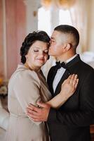 madre aiuta sua adulto figlio preparare per il nozze cerimonia. un emotivo e toccante momento a un' nozze. un' madre abbracci sua figlio foto